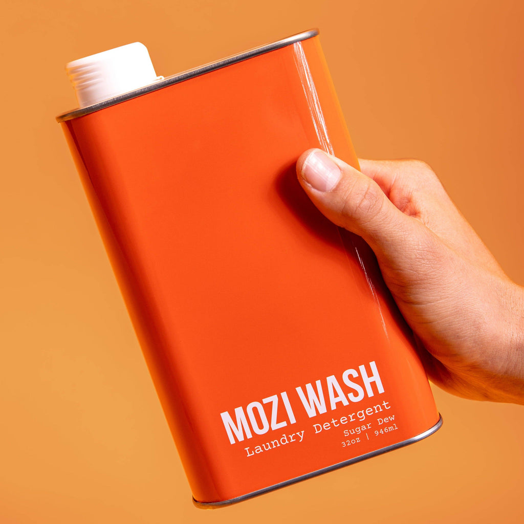 Orange can of Mozi Wash laundry detergent held by a hand against an orange background