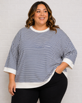 A woman wearing a navy and white horizontally striped knit top with white ribbed trim, paired with black pants, standing against a white brick wall.