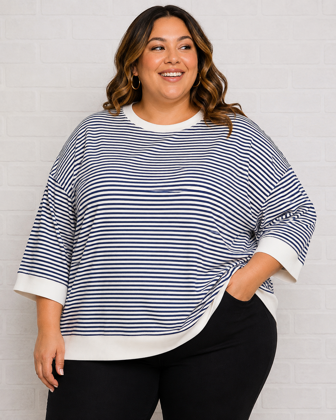 A woman wearing a navy and white horizontally striped knit top with white ribbed trim, paired with black pants, standing against a white brick wall.