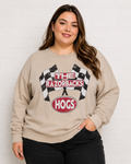 A woman wearing a beige crewneck sweatshirt with a 'The Razorbacks Hogs' racing graphic, paired with black pants, standing against a white brick wall.