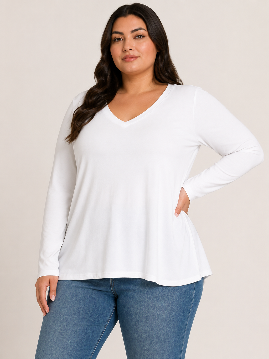 A woman modeling a white long-sleeve V-neck top with a flared hem, paired with blue jeans, against a plain light beige studio background.
