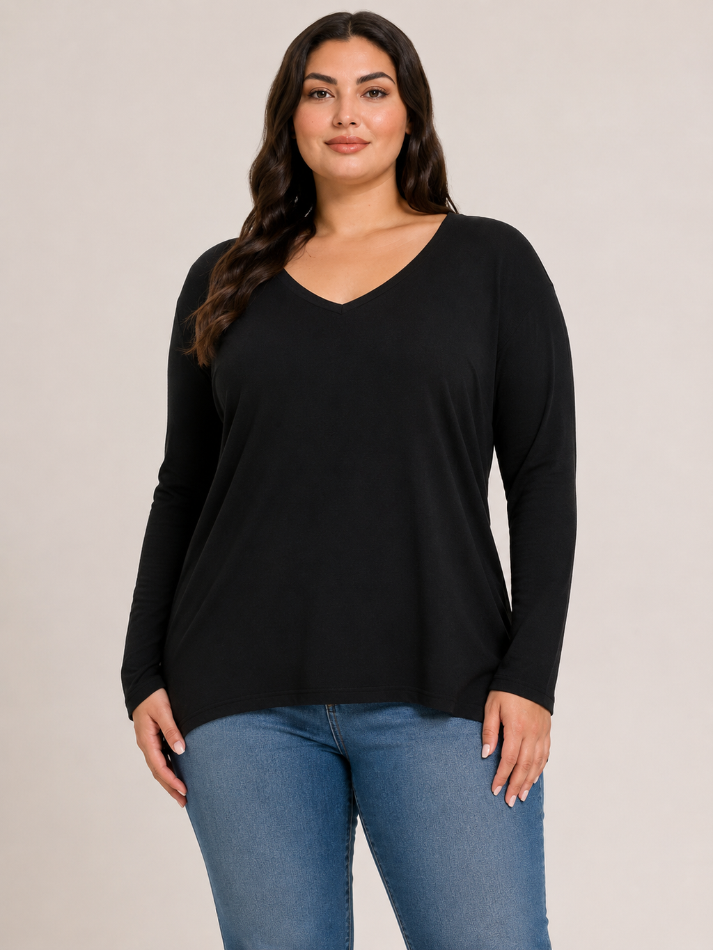 A woman modeling a black long-sleeve V-neck top with blue jeans against a plain light beige studio background.