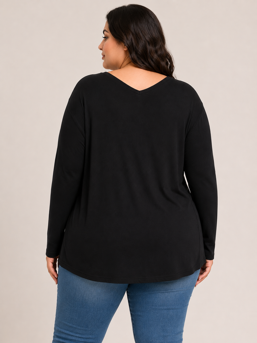 A woman shown from the back wearing a black long-sleeve top with a V-neckline and blue jeans, photographed against a plain light beige studio background.