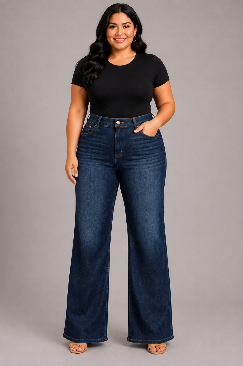 A woman modeling a pair of dark blue wide-leg jeans with a black short-sleeve t-shirt, standing against a solid gray studio background.