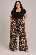 A woman modeling wide-leg leopard print pants with red side stripes, paired with a black short-sleeve top, against a solid light gray studio background.
