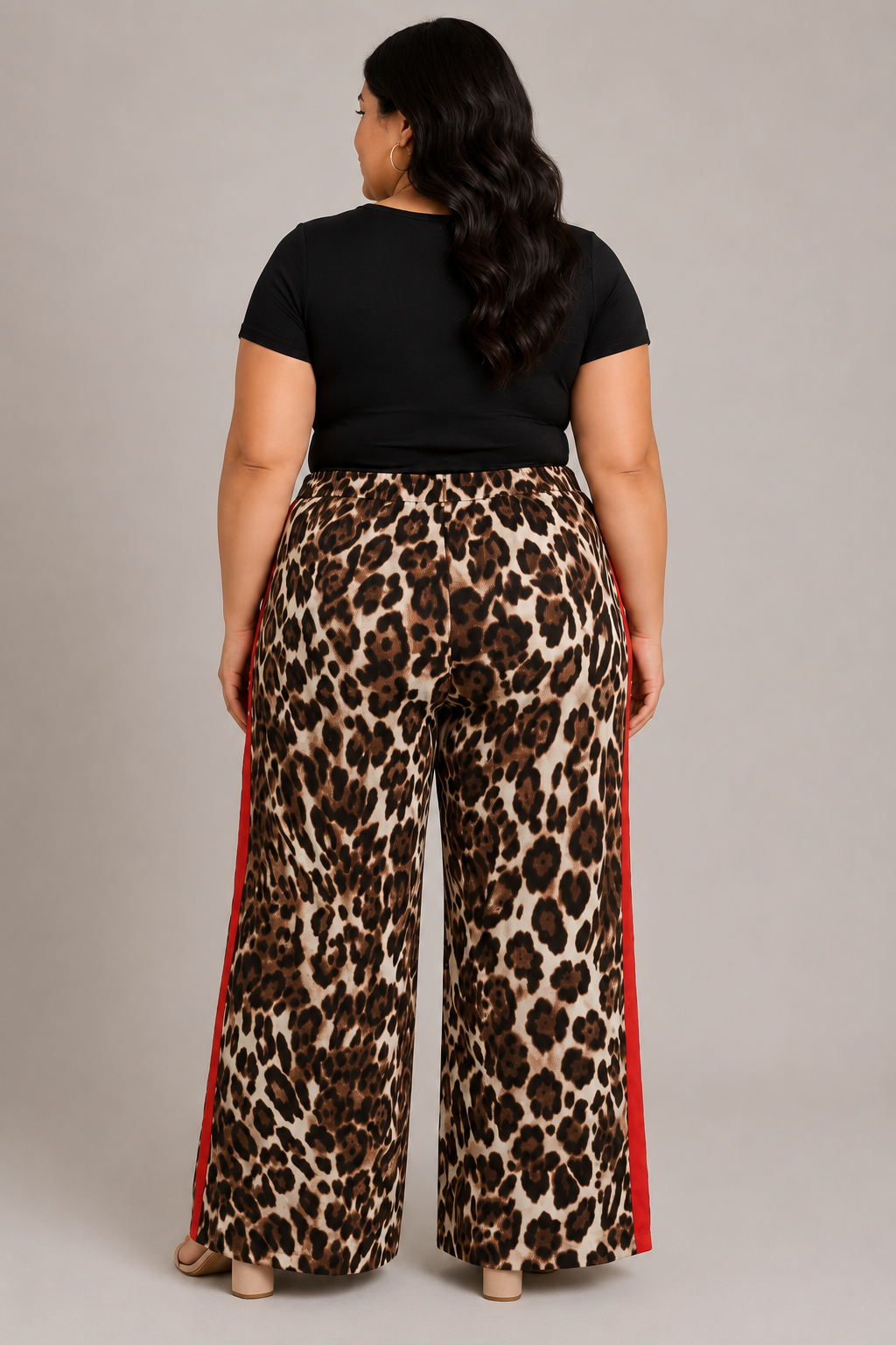 A woman shown from the back wearing leopard-print wide-leg pants with red side stripes, paired with a black short-sleeve top, against a plain light gray studio background.
