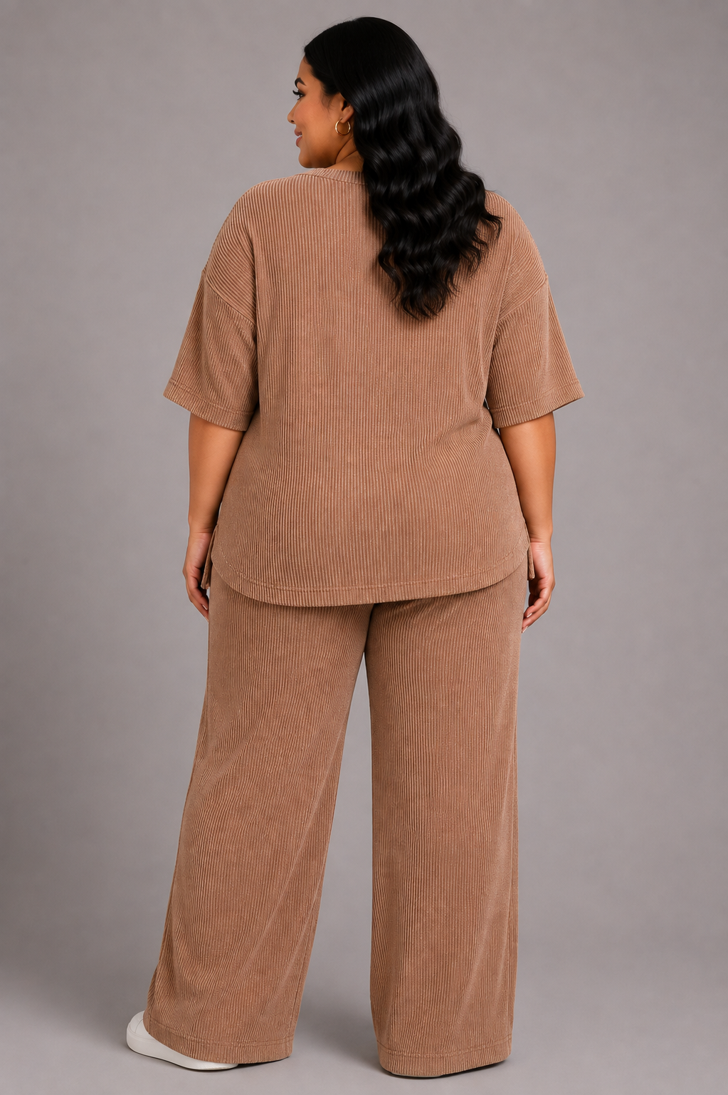 A woman viewed from the back wearing a matching two-piece lounge set in a warm tan corduroy fabric, consisting of a short-sleeve top and wide-leg pants, against a solid gray studio background.