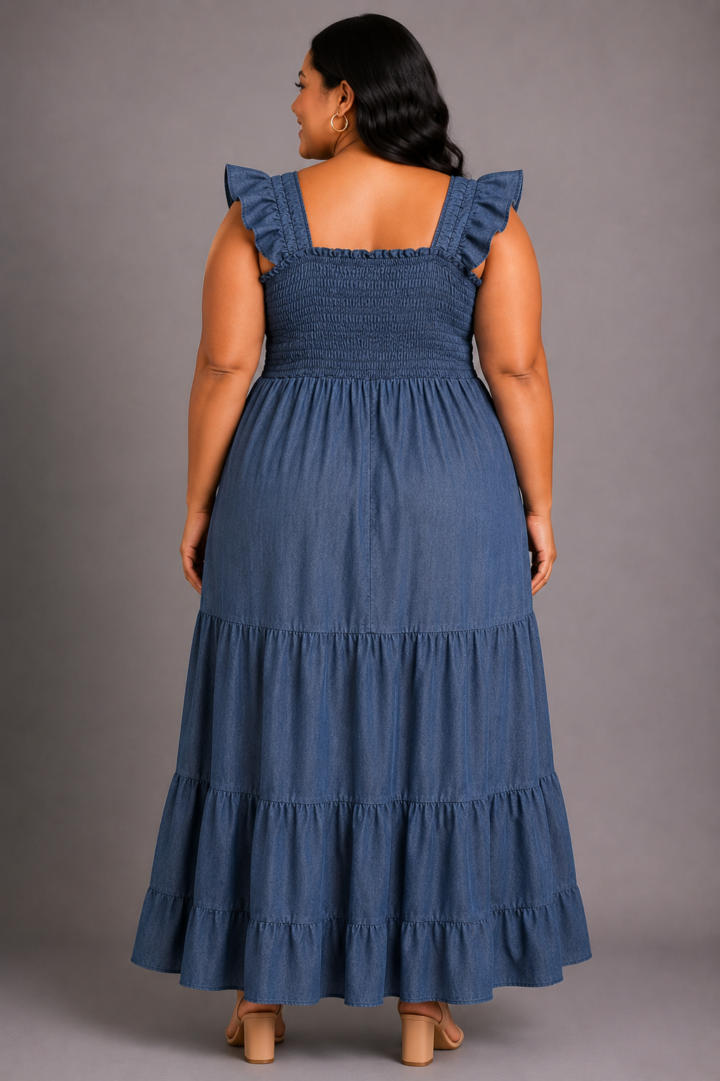 A woman wearing a blue tiered smocked maxi dress with ruffled shoulder straps, shown from the back against a solid gray studio background.