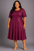 A woman modeling a short-sleeve, knee-length A-line dress covered in shimmering metallic sequins. The dress is a deep magenta-purple color with a sparkling texture, paired with nude high-heeled sandals, set against a solid gray studio background.