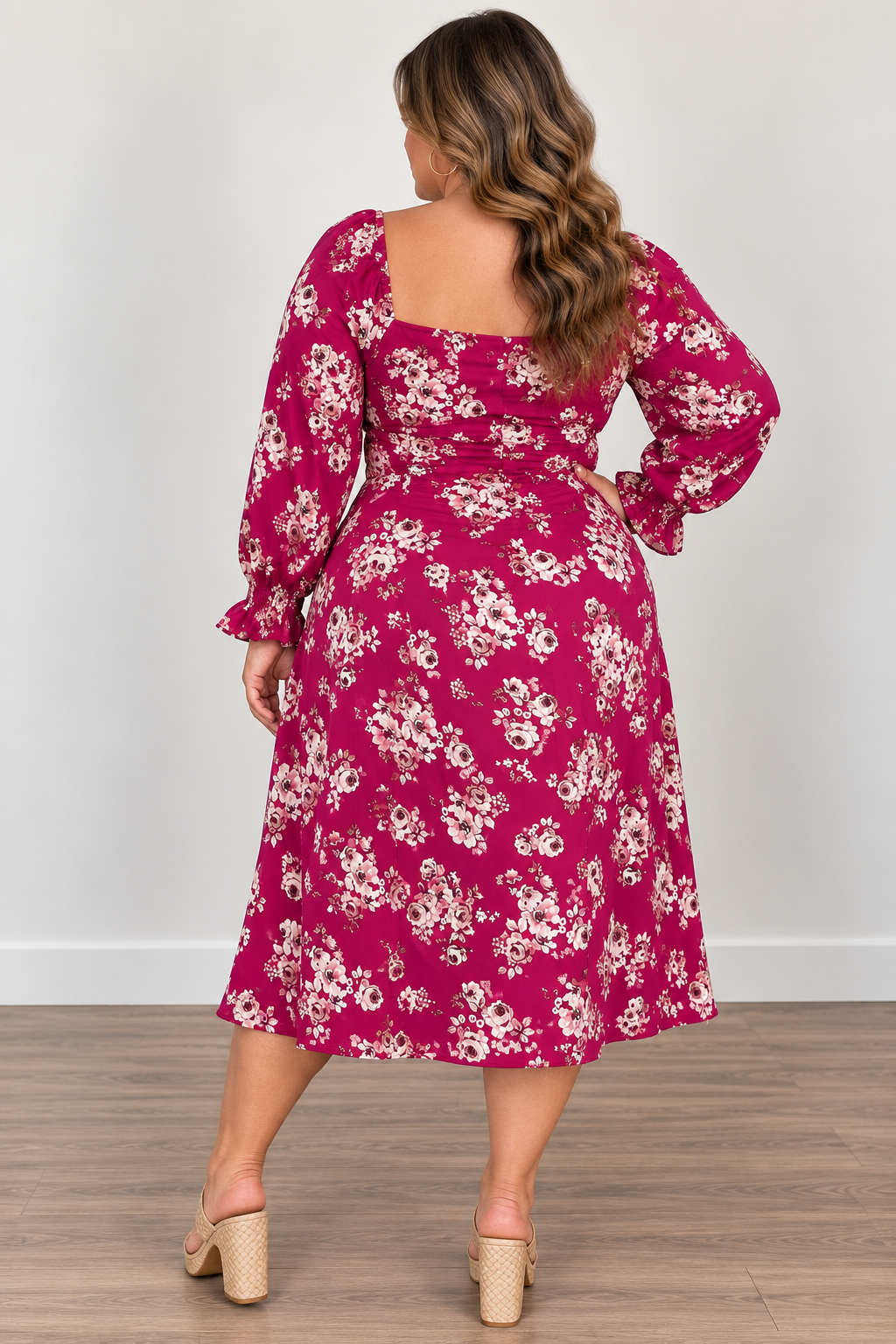 A woman wearing a long-sleeve midi dress with a floral print, shown from the back. The dress is a vibrant magenta pink with a white and light pink floral pattern.
