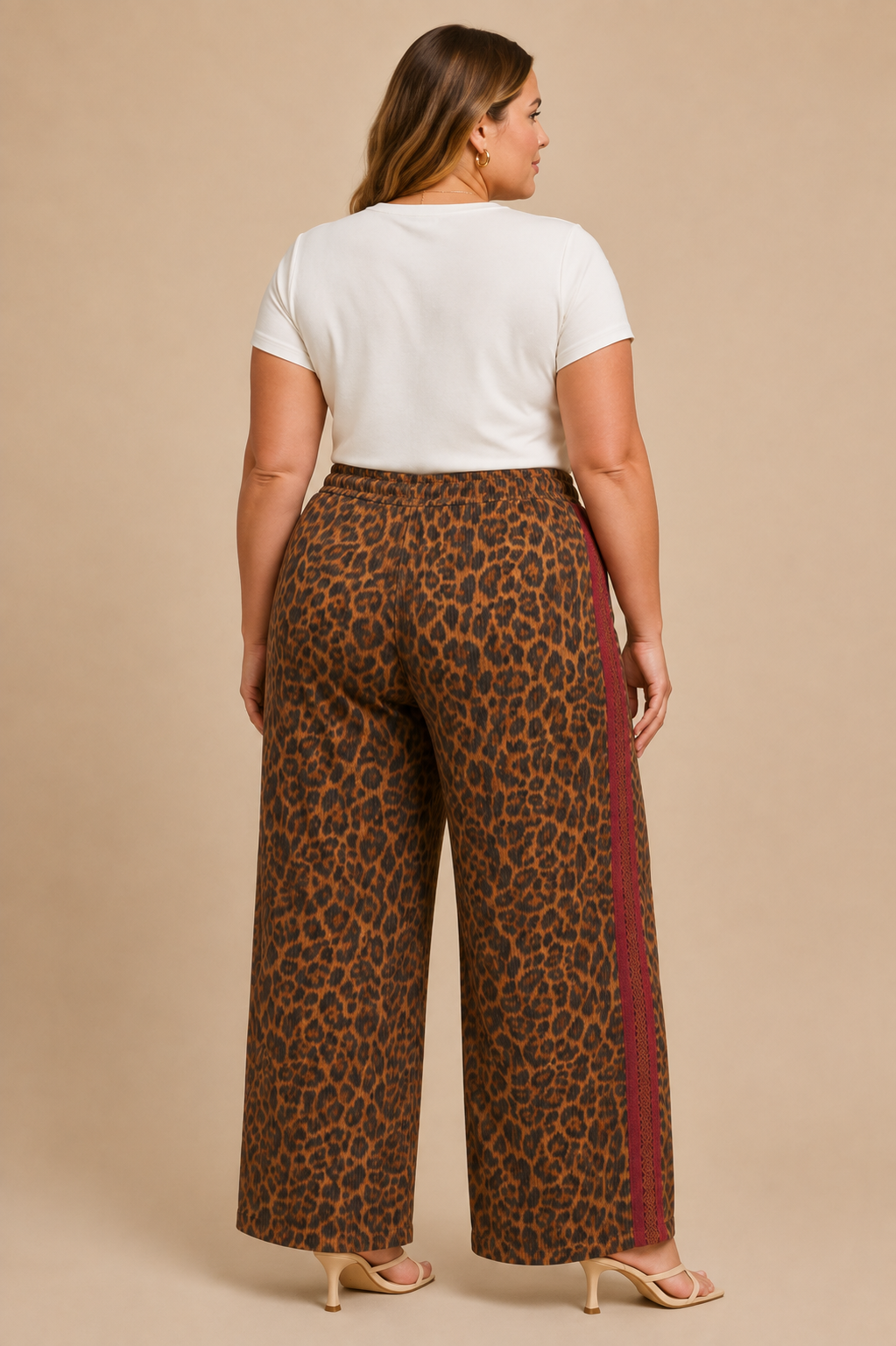 A woman shown from the back wearing leopard-print wide-leg pants with a rust-colored side stripe, paired with a white short-sleeve top and beige heels, against a solid beige studio background.