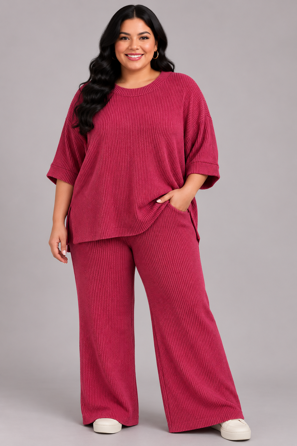 A woman modeling a matching ribbed knit lounge set in a deep magenta pink, featuring a short-sleeve top and wide-leg pants, against a solid gray studio background.